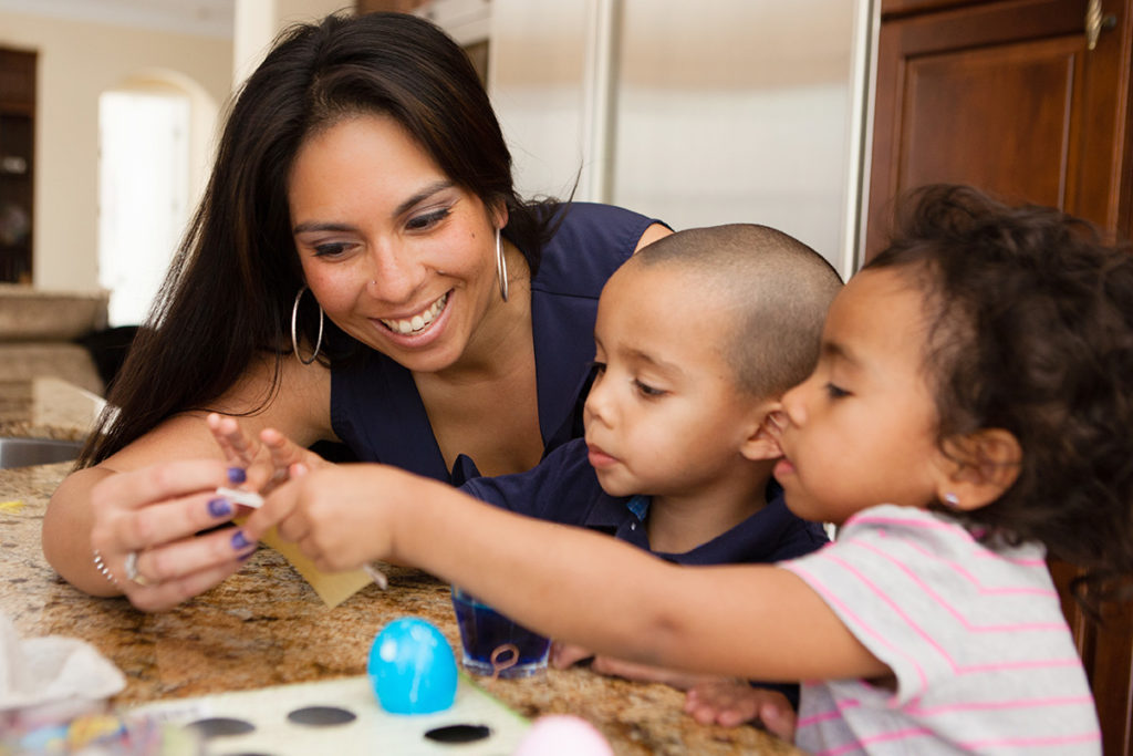 Mother coloring Easter eggs with her two young children.