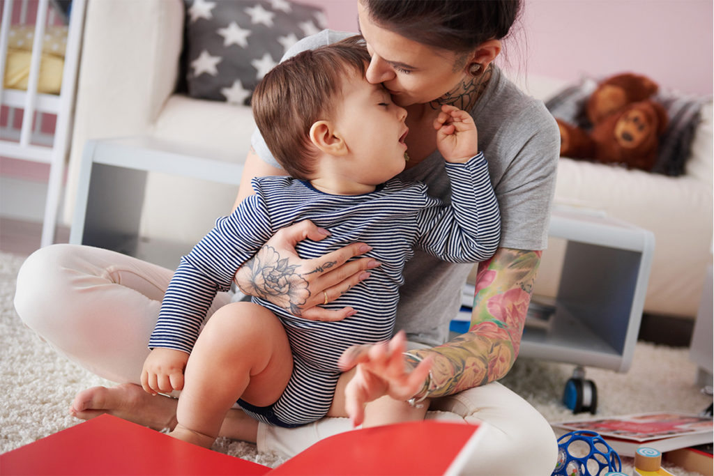 Mom with tattooed arm holding and kissing child.