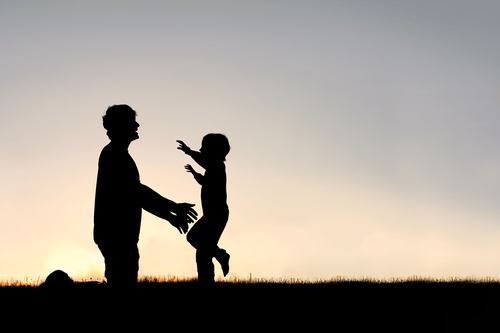Silhouette of happy young child running to greet dad.