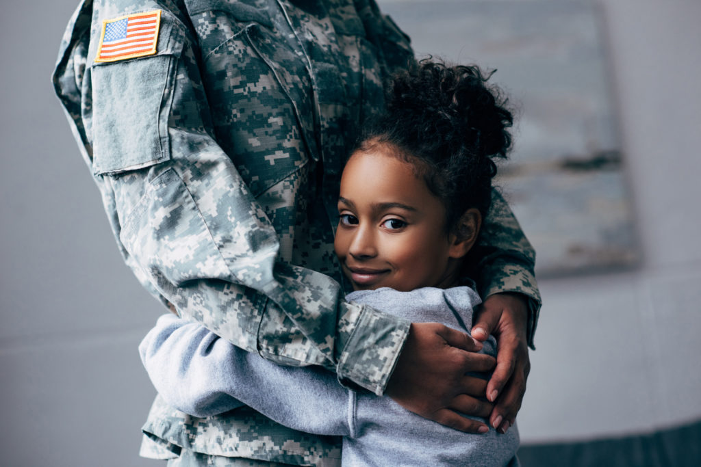 Preteen daughter hugging parent in military uniform.