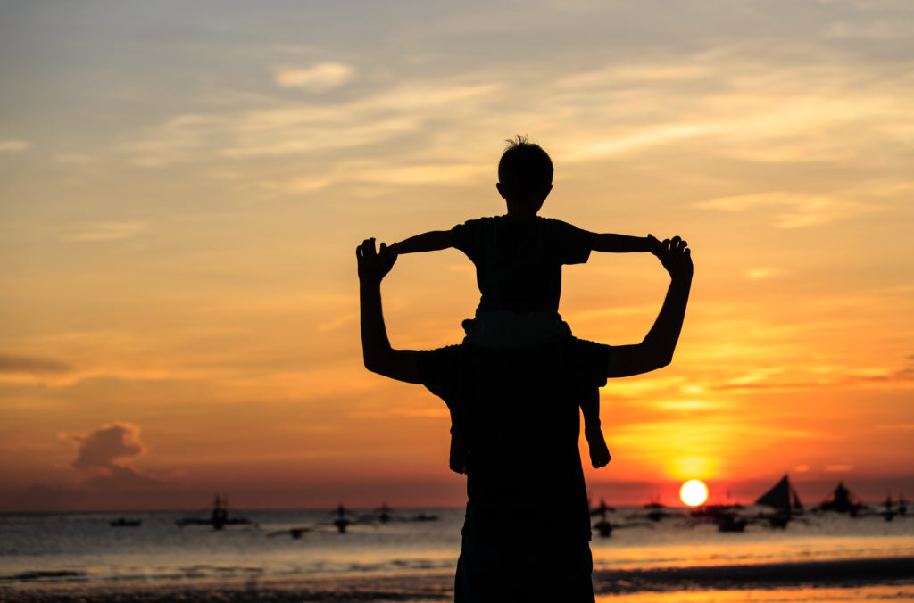 Silhouette of child on adult's shoulders at sunset.