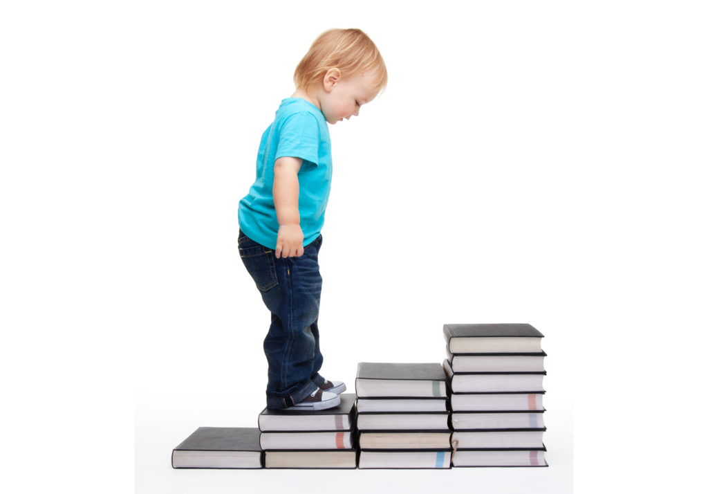 Child standing on books arranged as steps.