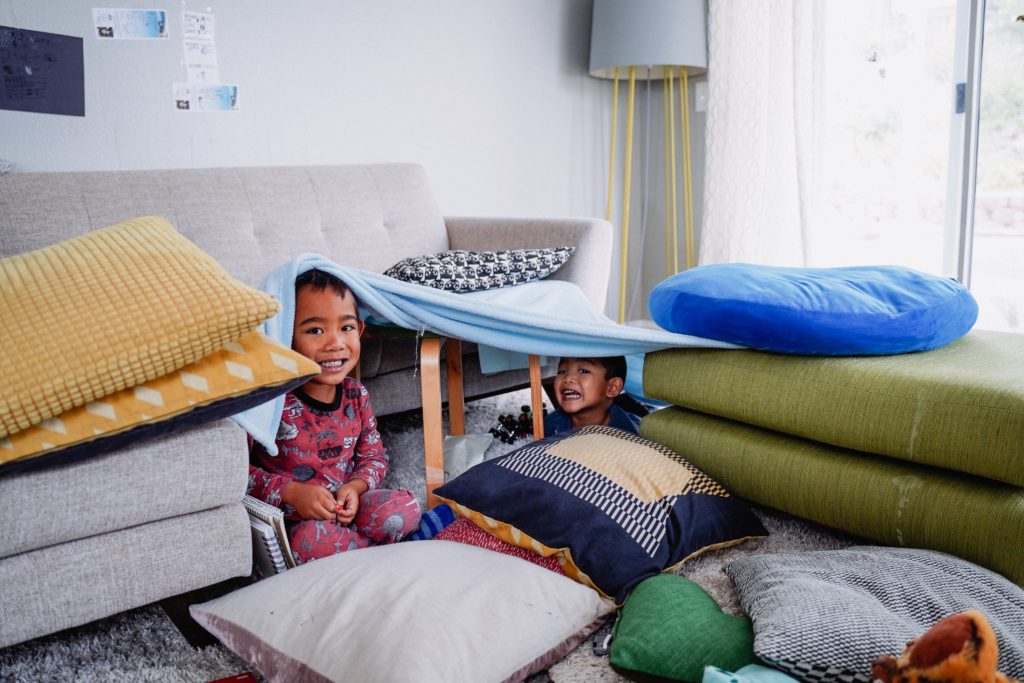 Siblings playing in a pillow and blanket fort.