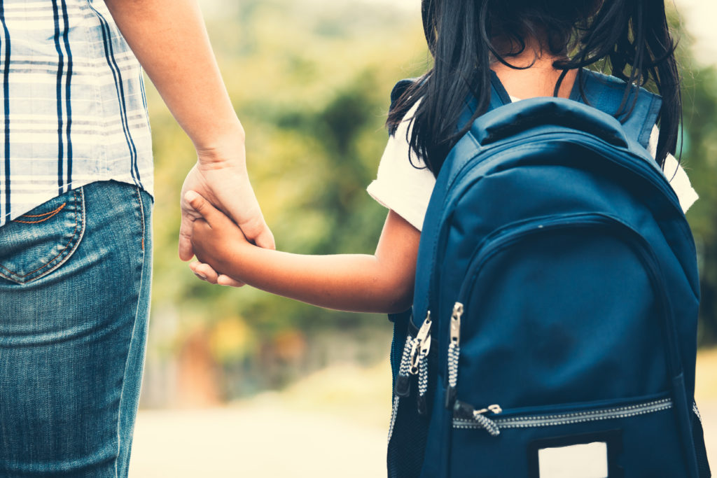 Child wearing a backpack holding an adult's hand.
