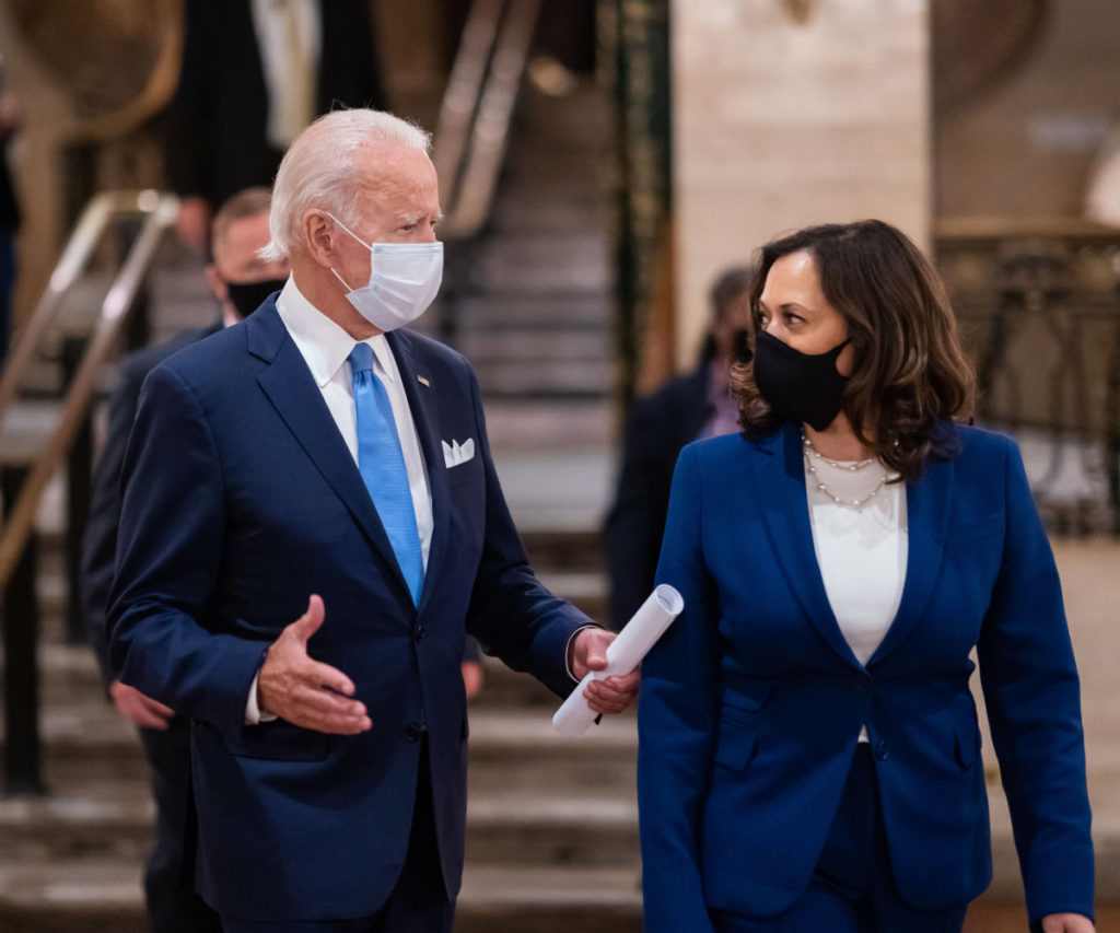 President Joe Biden and VP Kamala Harris talking while wearing masks.