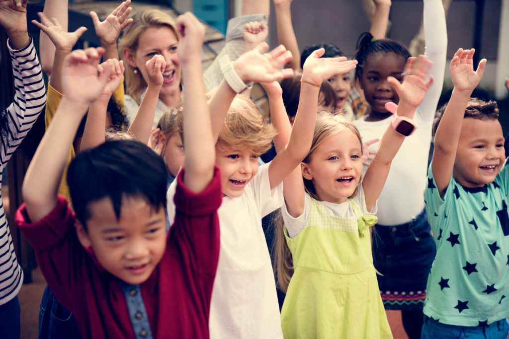 Group of young children smiling with raised hands.