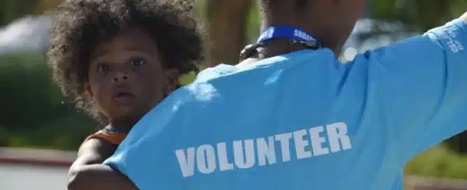 Woman with shirt reading "Volunteer" holding a child.
