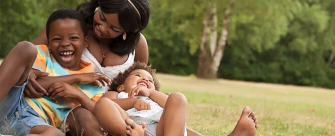 Mother laughing with her two kids in the grass.