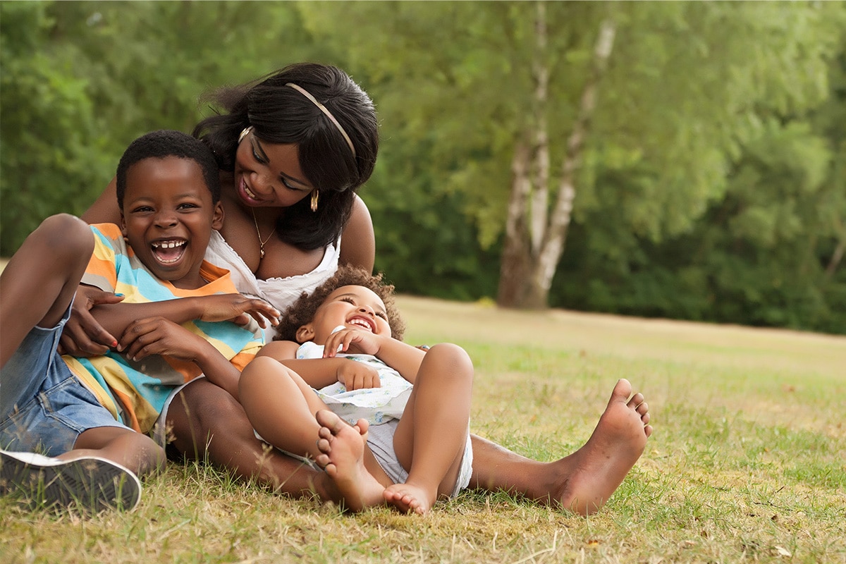 Mother laughing with her two kids in the grass.