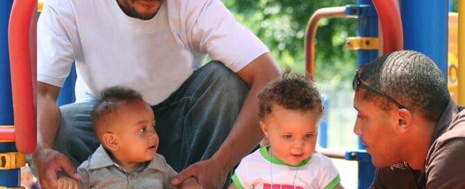 Two black fathers playing with their children at the playground.