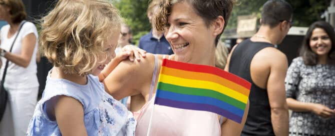 Mother holding daughter with a LGBTQIA+ flag.