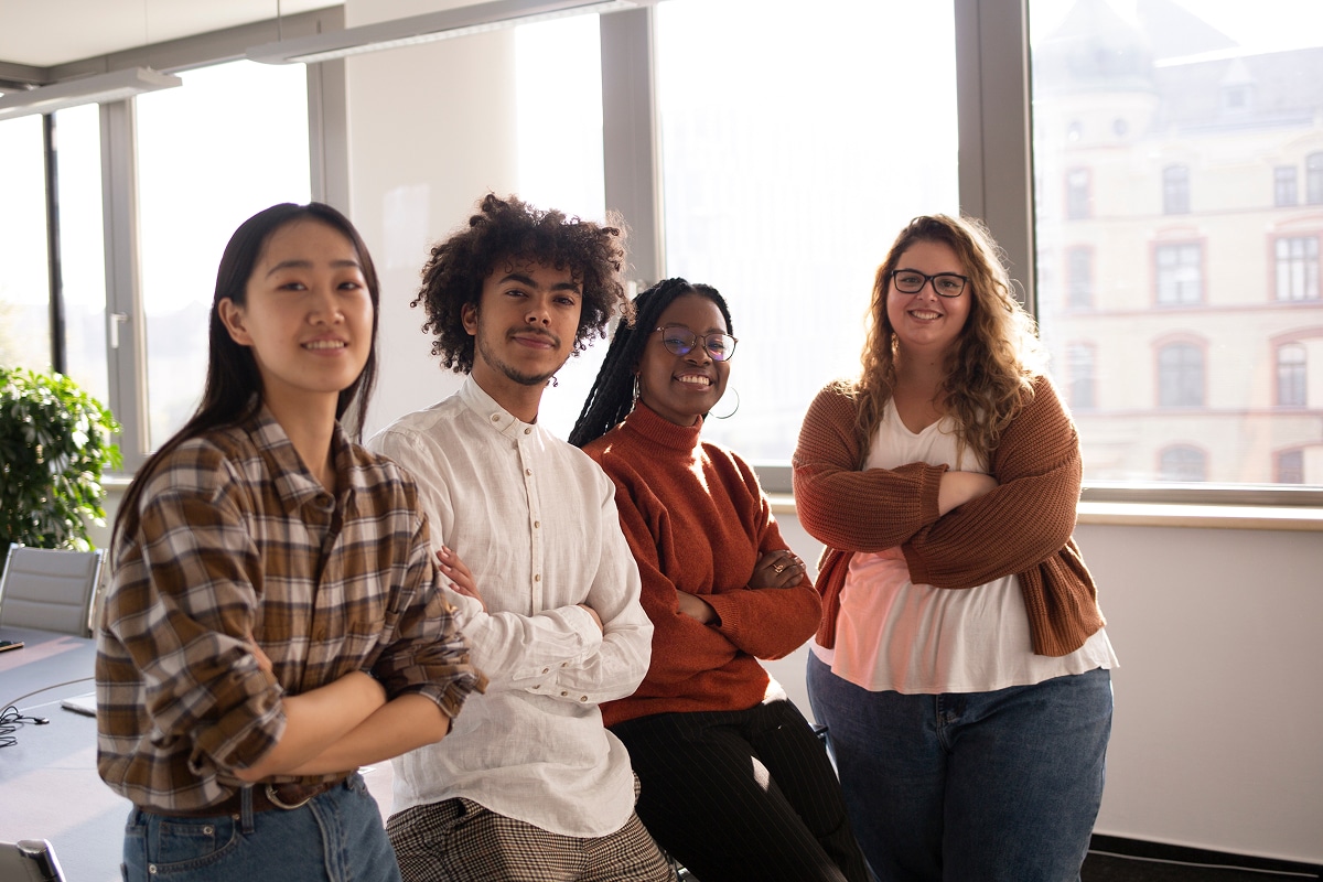 A multiracial group leaning on a table in front of windows.