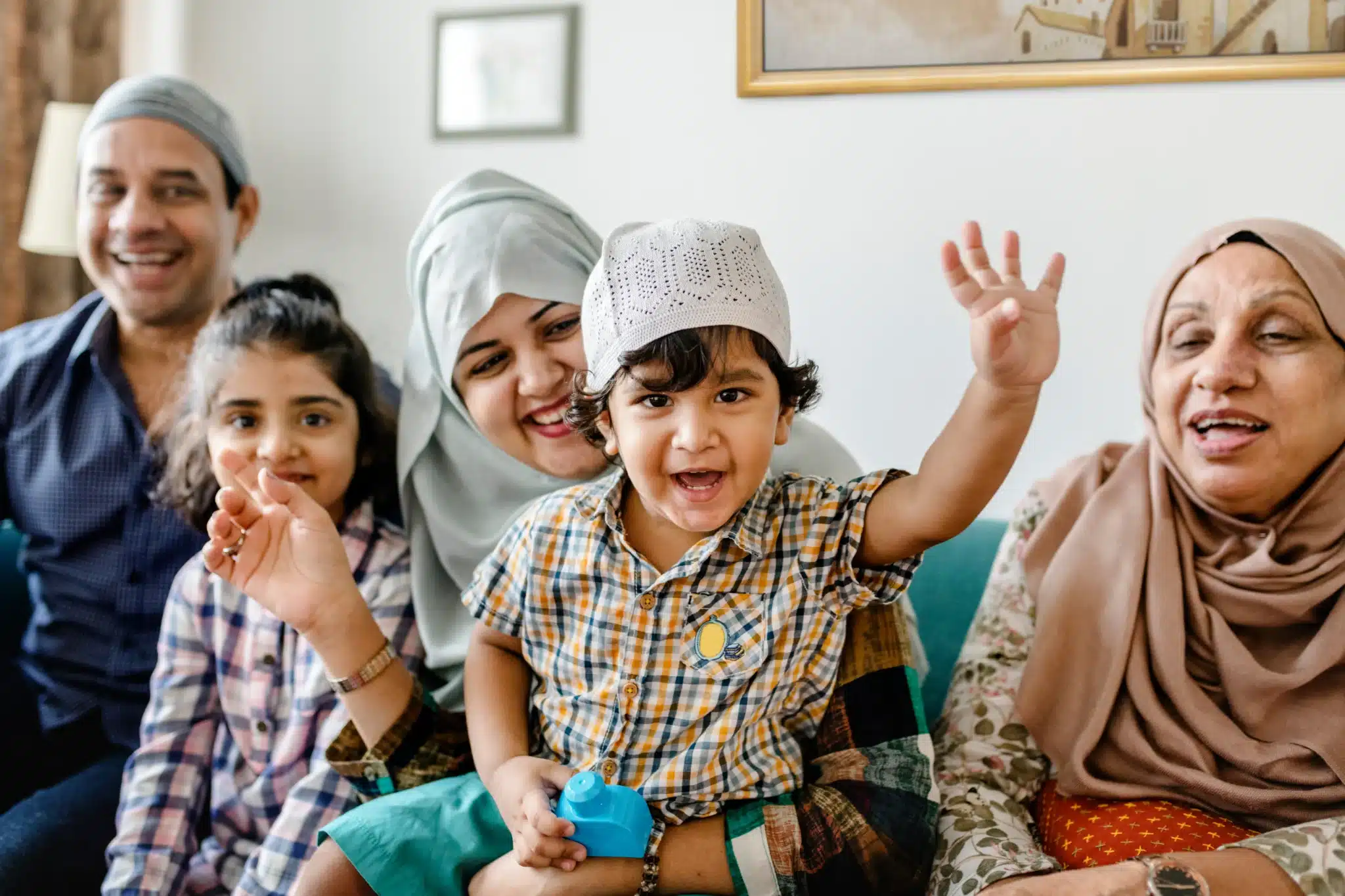 A family sitting on a couch together waving and smiling at the camera.