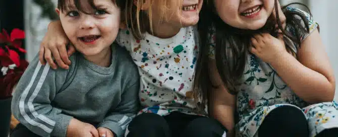 three kids with their arms around each other smiling