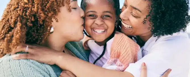 Family of women with their female child showing affection embracing in a hug outdoors.