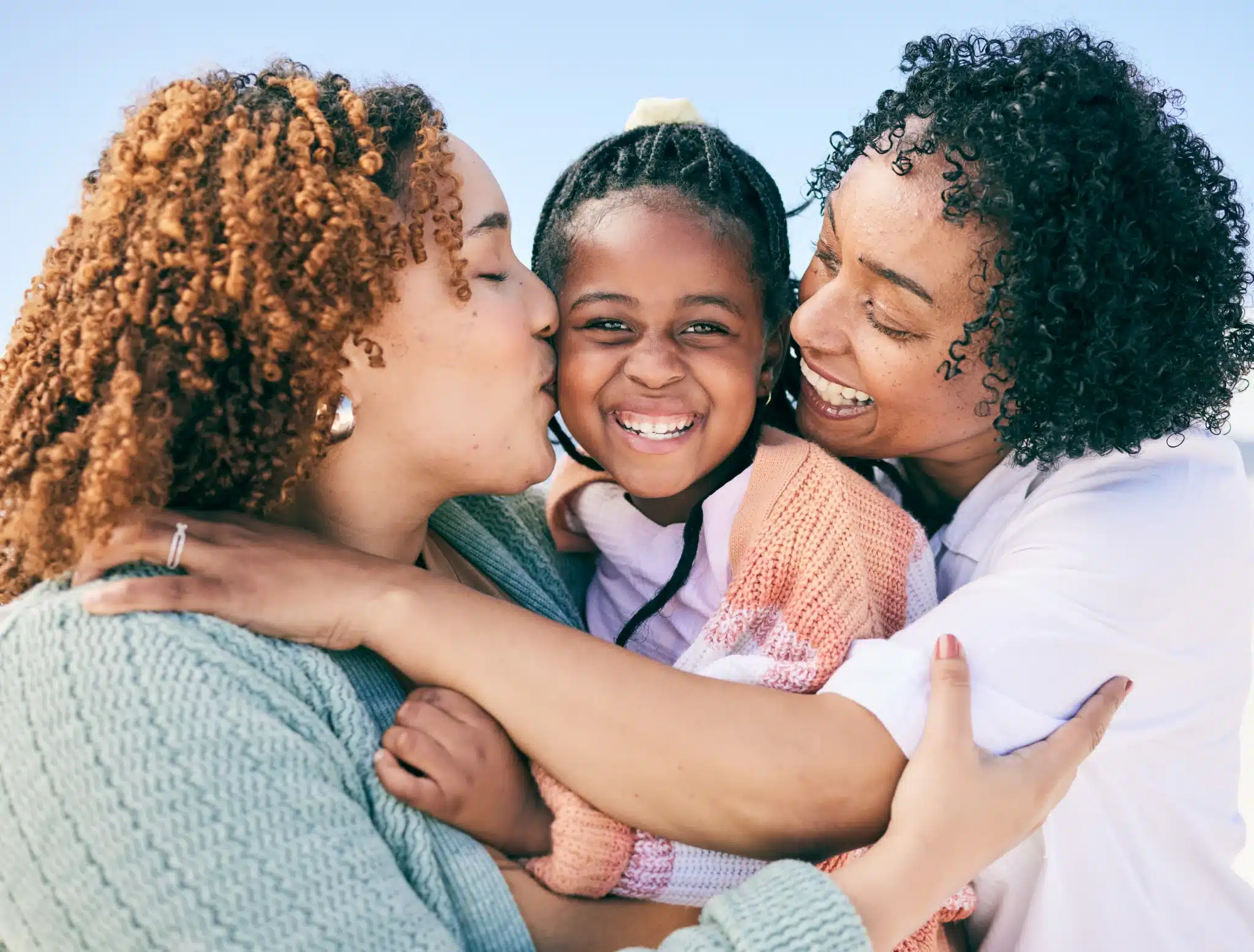 Family of women with their female child showing affection embracing in a hug outdoors.