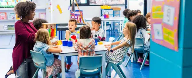 Diverse classroom with a teacher and children of various ethnicities learning together in a colorful classroom setting.