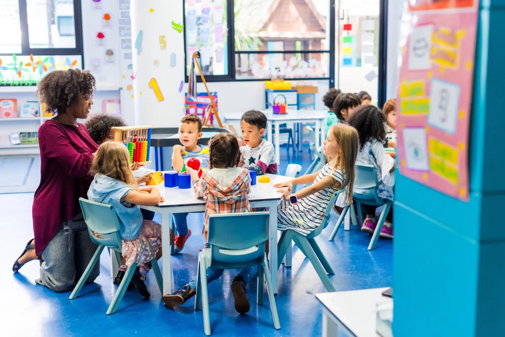 Diverse classroom with a teacher and children of various ethnicities learning together in a colorful classroom setting.